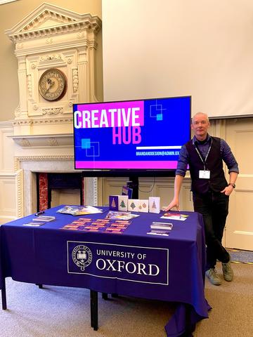 Mark Vice standing in front of a Oxford Creatives stand at a conference